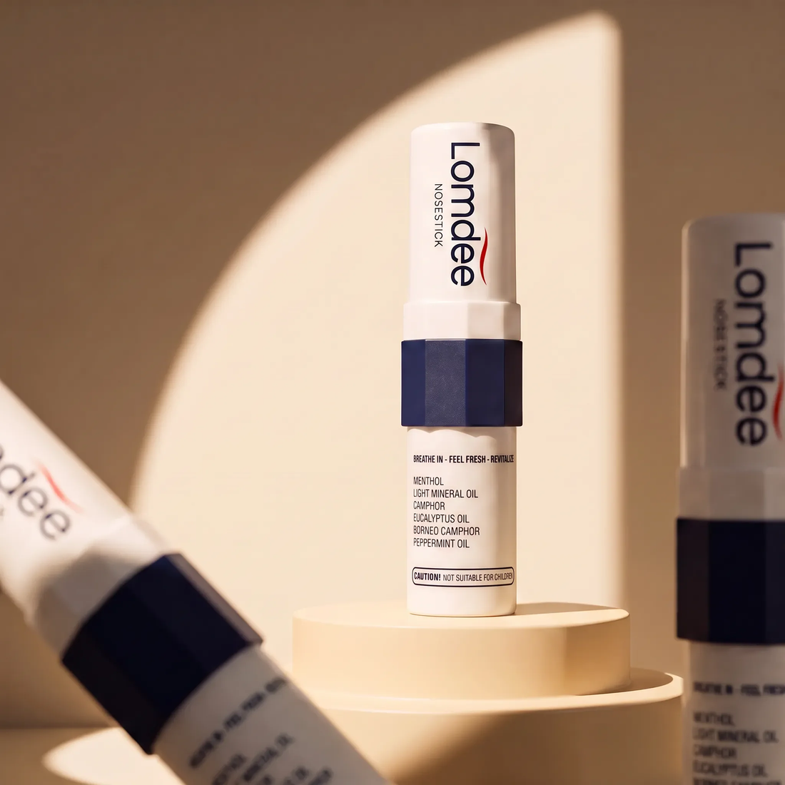 Lomdee Nosestick in Weiß und Dunkelblau auf einem Podest, daneben zwei weitere Sticks